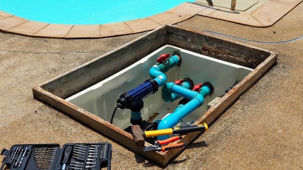 Arqueta técnica abierta con bomba, filtro y tuberías de una depuradora de piscina