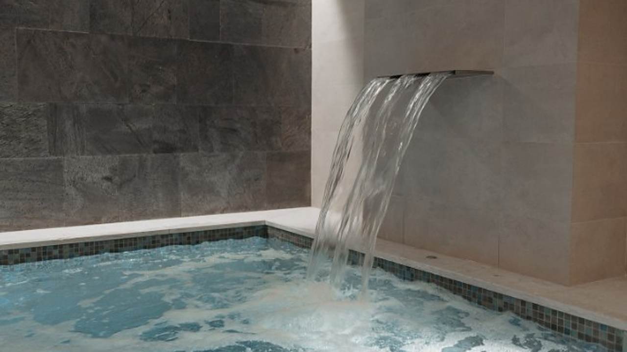 Spa de obra con hidromasaje y caño de agua sobre pared de piedra